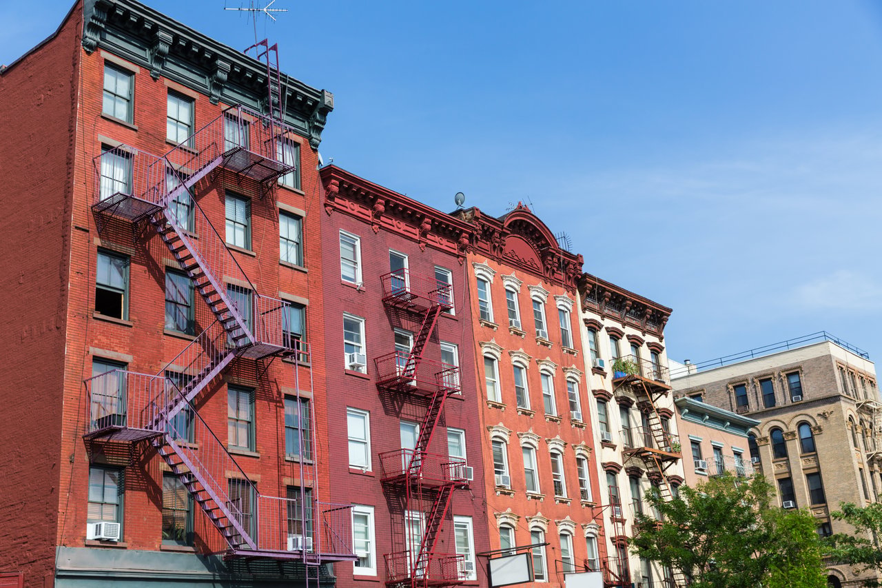 Multistory brick apartment buildings with ornate facades and metal fire escapes beneath a clear blue sky.