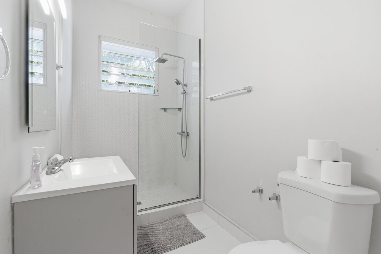 Bright bathroom with a glass-enclosed shower, gray vanity, and louvered windows.