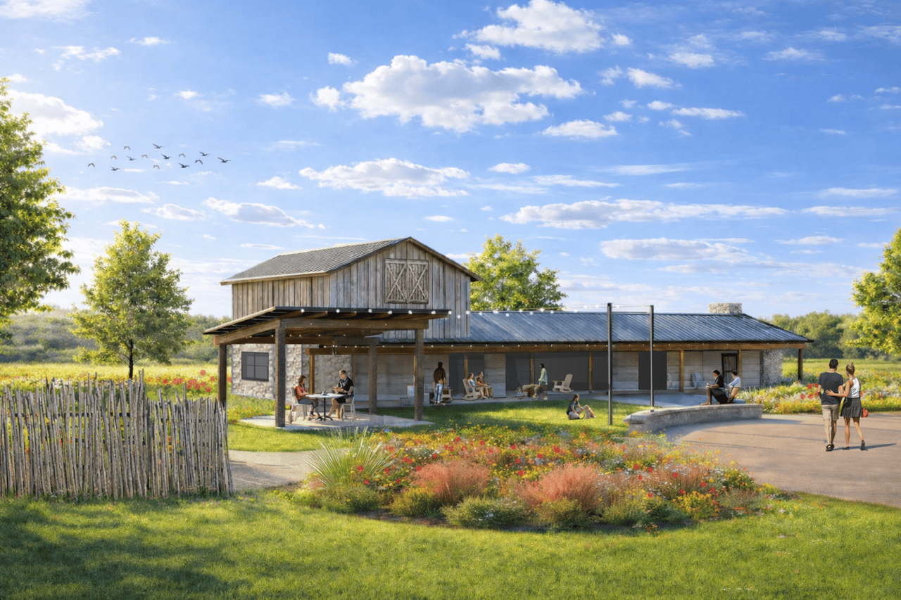 Community pavilion with a covered patio, stone-and-wood exterior, flower beds, and visitors outdoors.