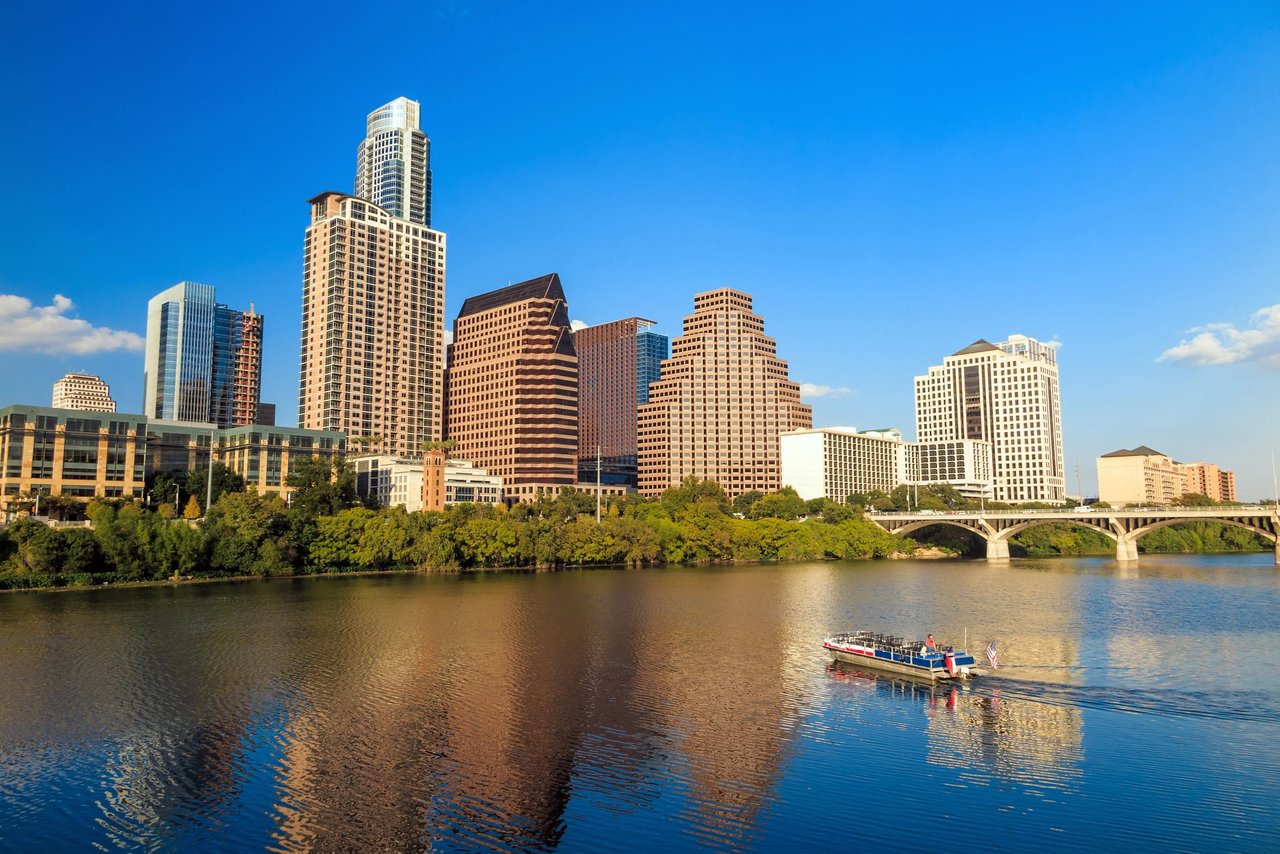 Downtown Austin skyline across the river, with a bridge and sightseeing boat.