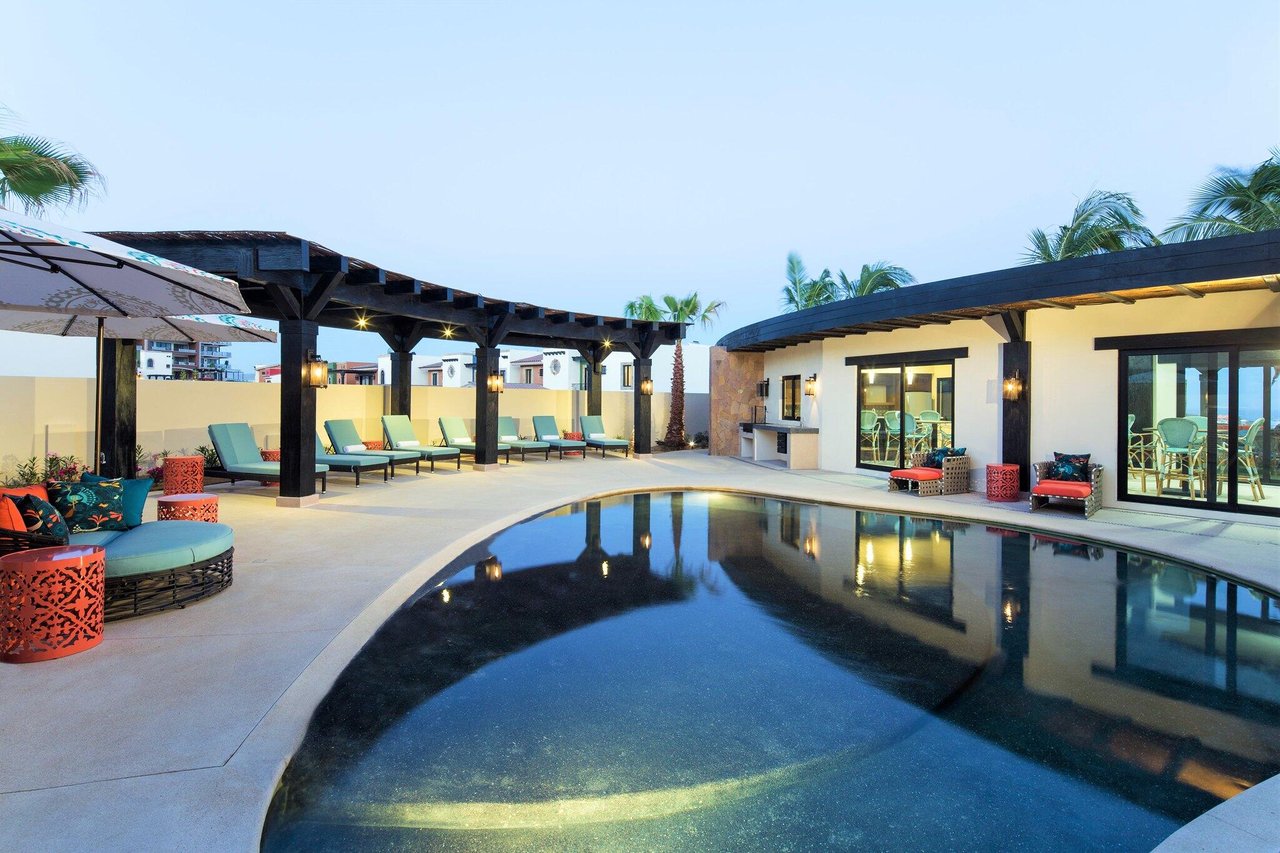Outdoor pool beside a clubhouse, with pergola-shaded lounge seating.