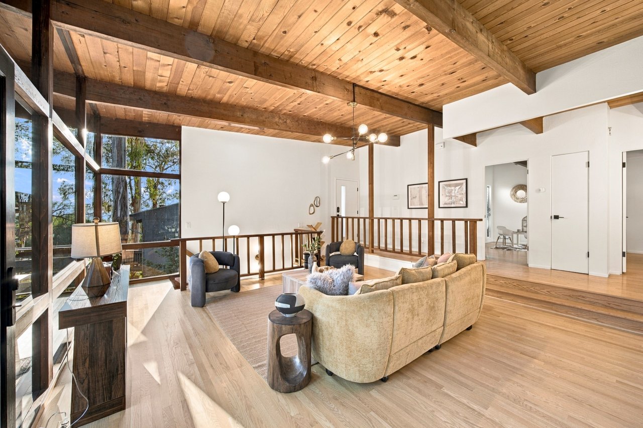 Living room with a vaulted wood ceiling, floor-to-ceiling windows, and a furnished seating area.