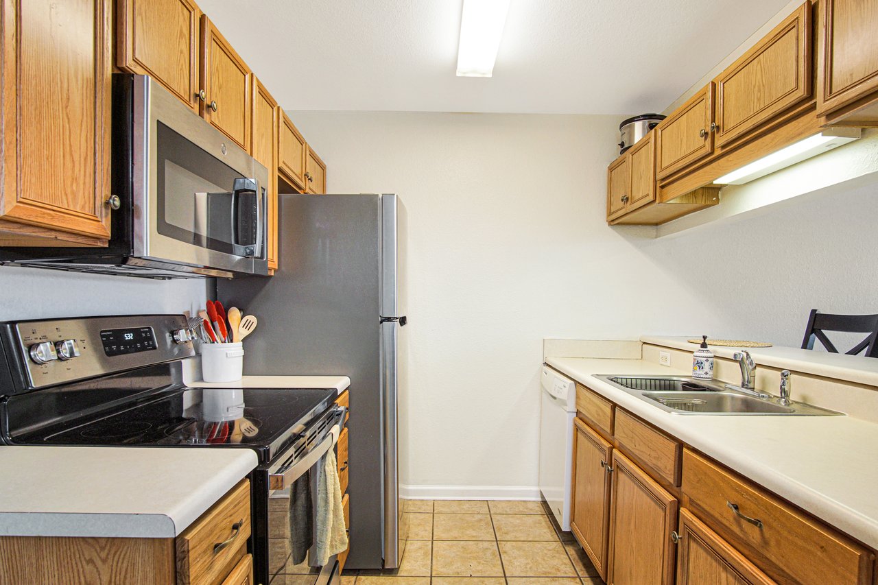 A tidy kitchen features wooden cabinetry, stainless steel appliances, and a bright atmosphere. A stovetop and sink enhance the cozy, functional space.