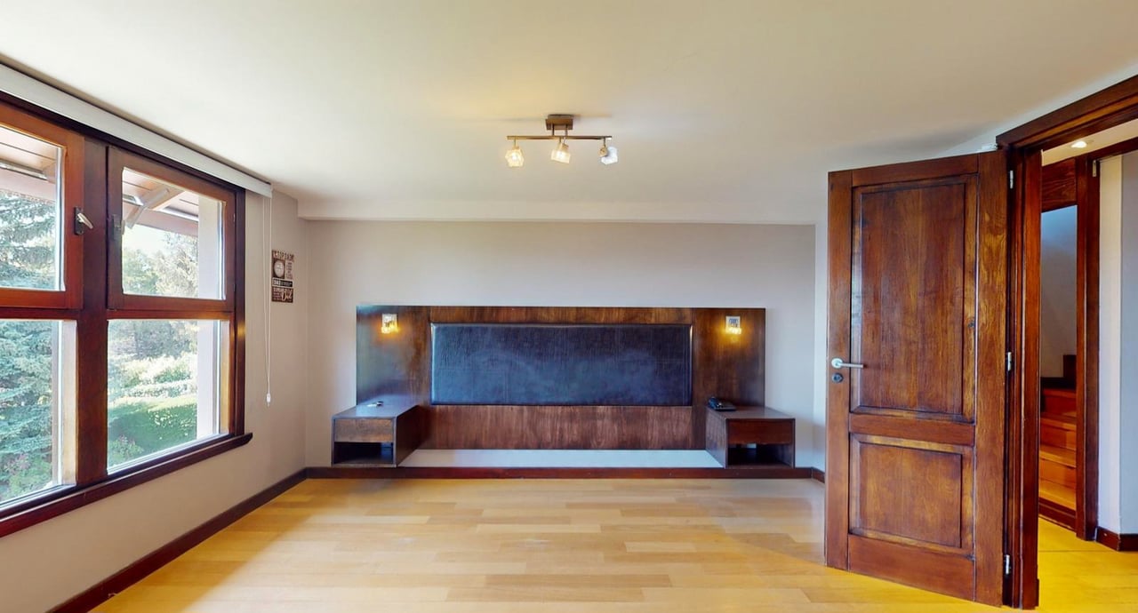 Vacant bedroom with a built-in dark wood headboard, light wood floor, and large windows.