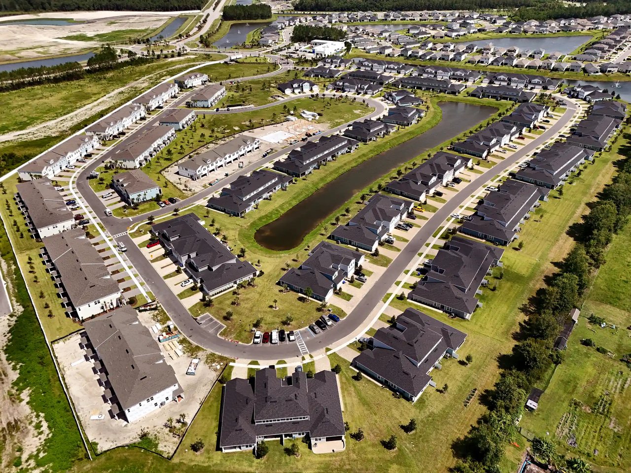 Aerial view of a residential development with curving streets, a retention pond, and homes under construction.