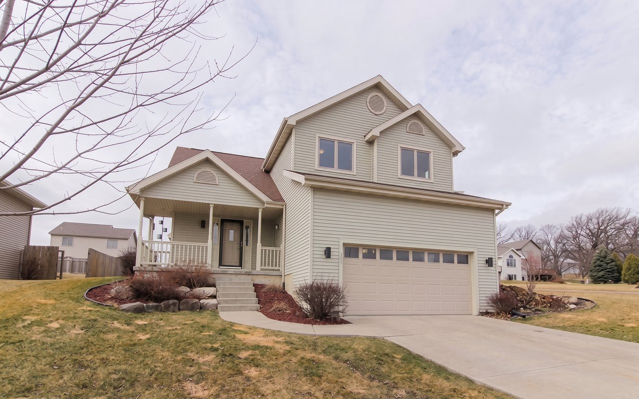 Two-story beige-sided home with an attached garage, covered porch, and curved driveway.