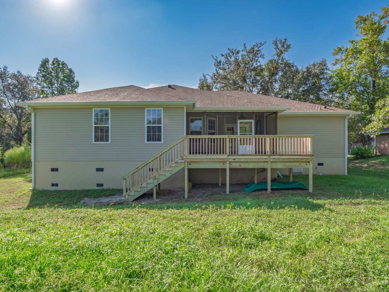 Rear of a pale green home with a raised wooden deck, stairs, and grassy yard.