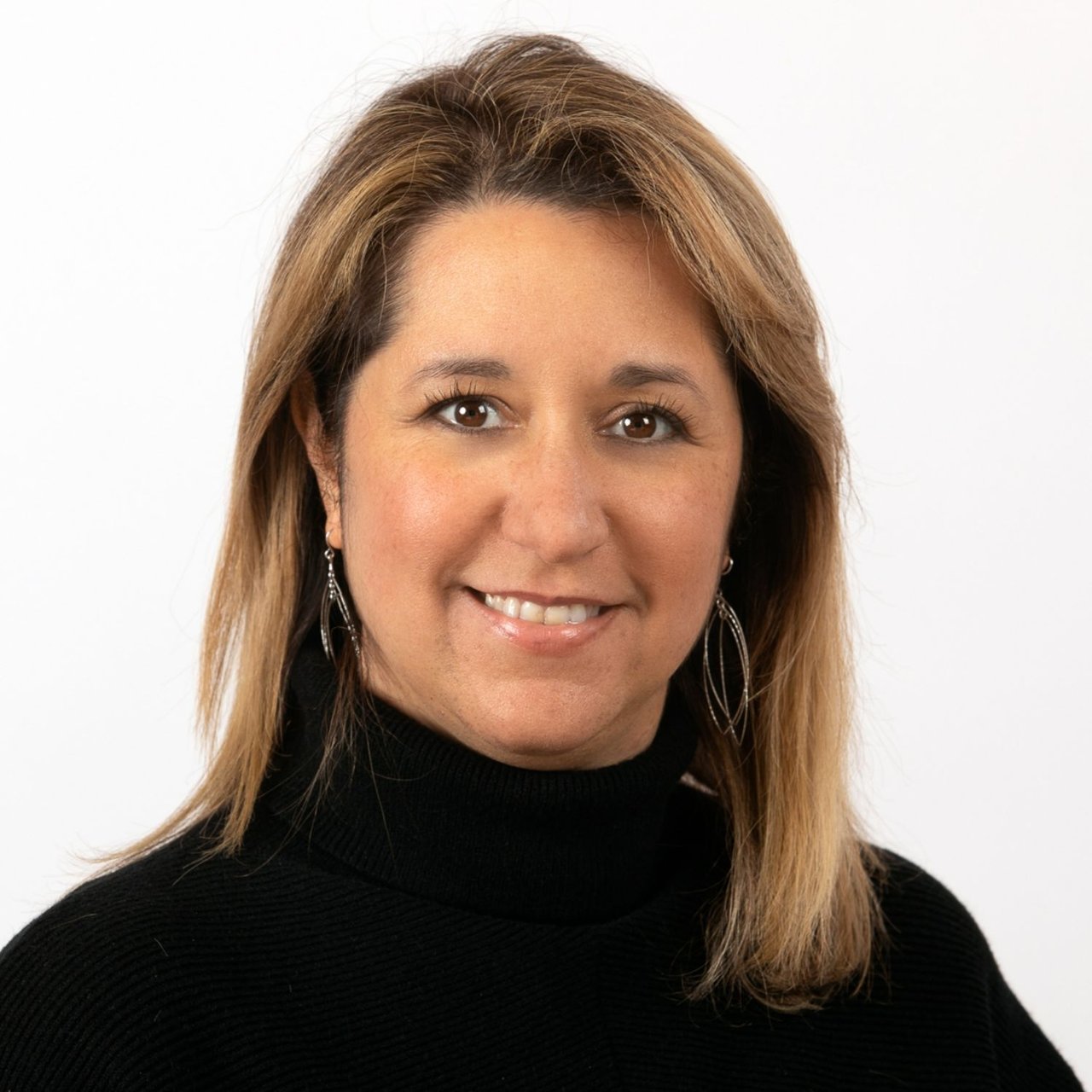 Joanne Guarino smiling in a black turtleneck and dangling earrings.