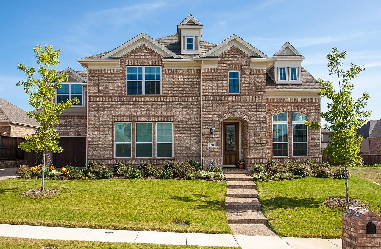 Two-story brick home with multiple gables, a landscaped front lawn, and a central walkway.