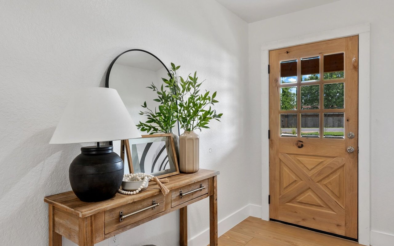 Entryway with a carved wood-and-glass front door and console table topped with a lamp and greenery.