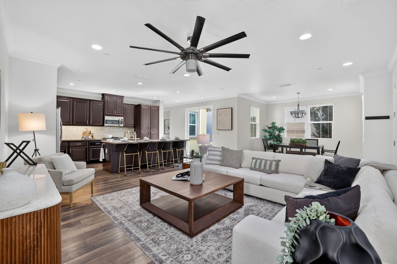 Open-plan living room with a white sectional, dark wood kitchen, and oversized ceiling fan.