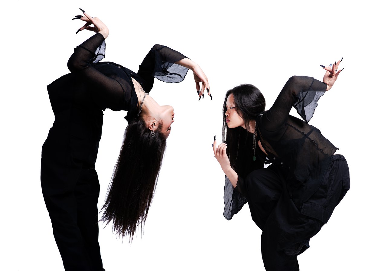 Two dancers in black pose together, one bending backward and the other crouching with an arm raised.