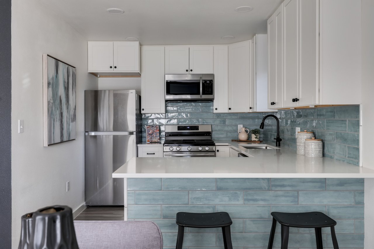 Kitchen with white cabinets, stainless steel appliances, blue-green tile, and a peninsula with two black stools.