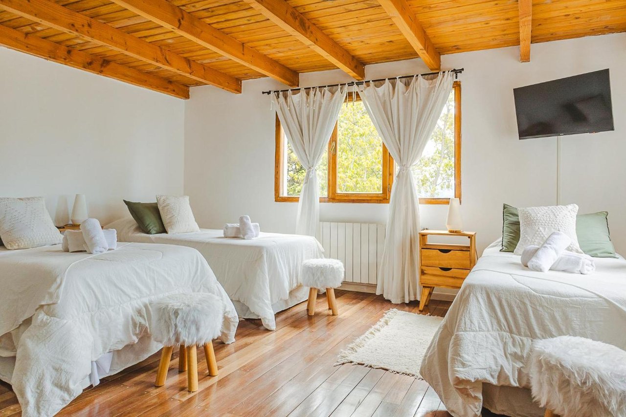 Hotel bedroom with white-covered beds, exposed timber ceiling, and a sunlit window.
