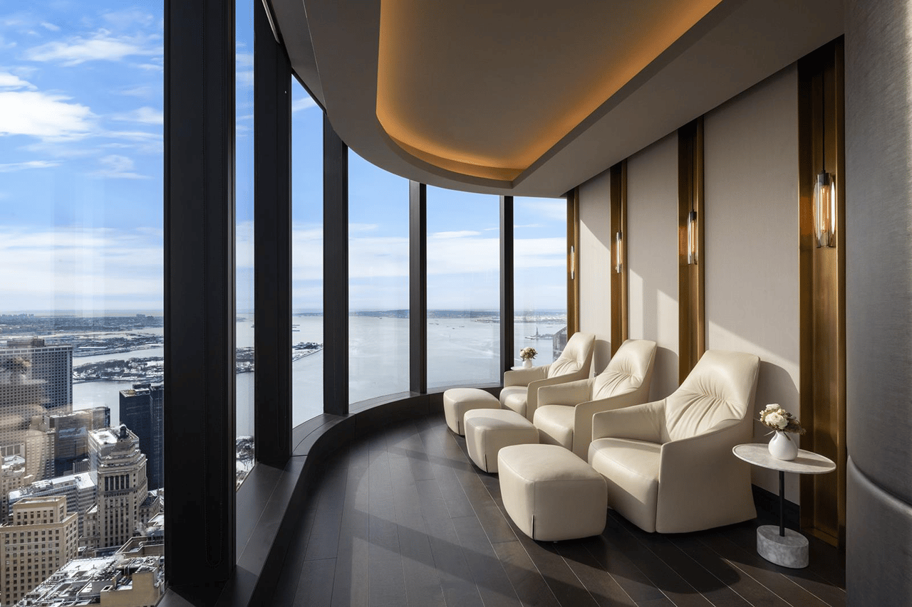 High-rise lounge with cream reclining chairs and floor-to-ceiling windows overlooking the water and city skyline.