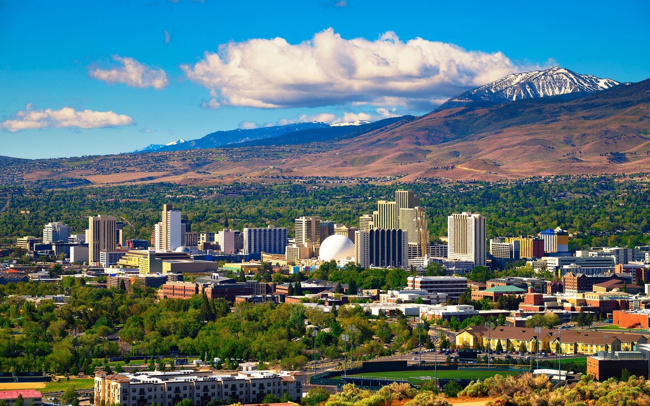 Downtown Reno skyline and neighborhoods below snow-dusted Sierra Nevada mountains.