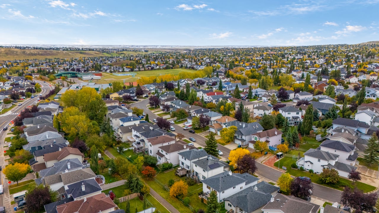 Aerial view of a residential neighborhood with autumn-colored trees and sports fields in the distance.