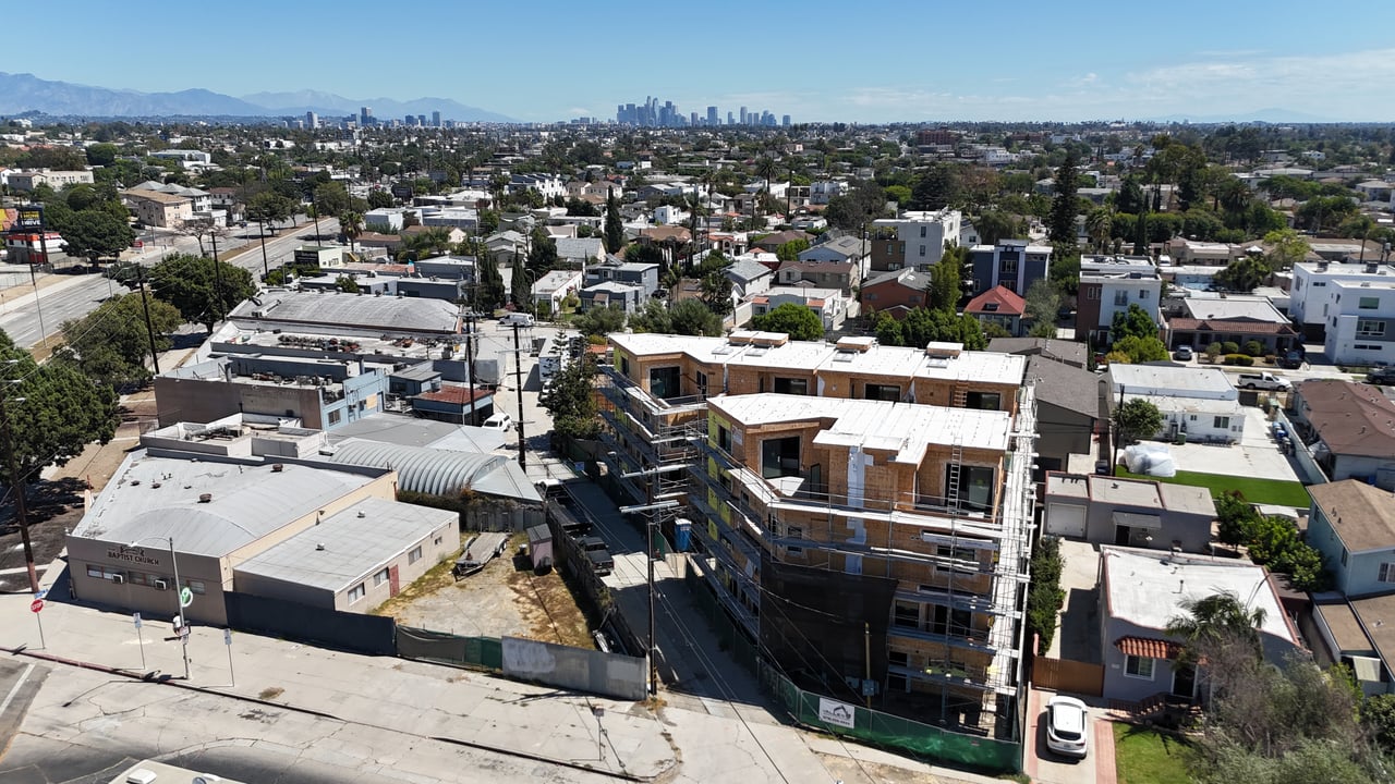 Aerial view of a multifamily building under construction with the downtown Los Angeles skyline beyond.