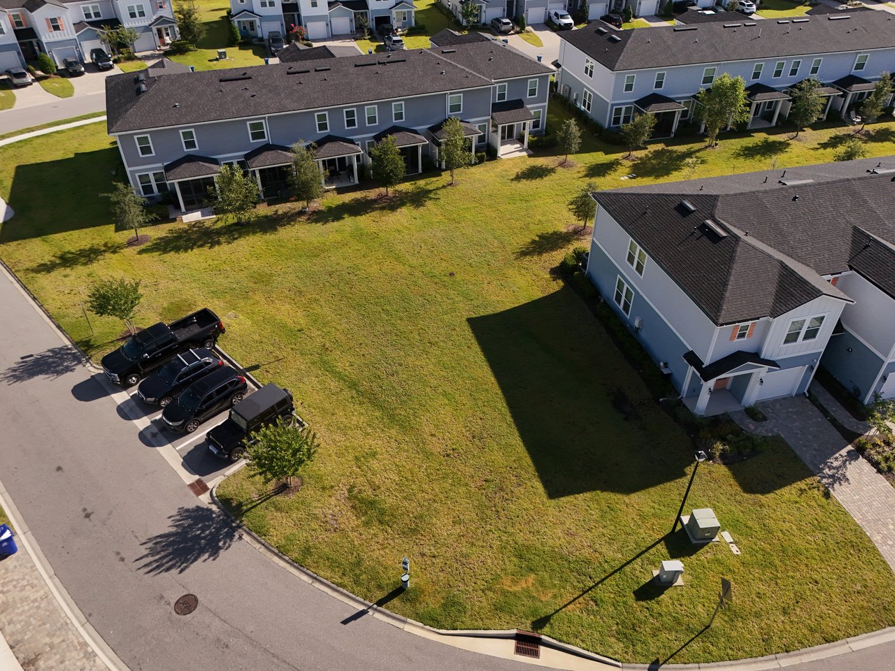 Aerial view of townhomes around a broad grassy courtyard, with parked vehicles along the street.