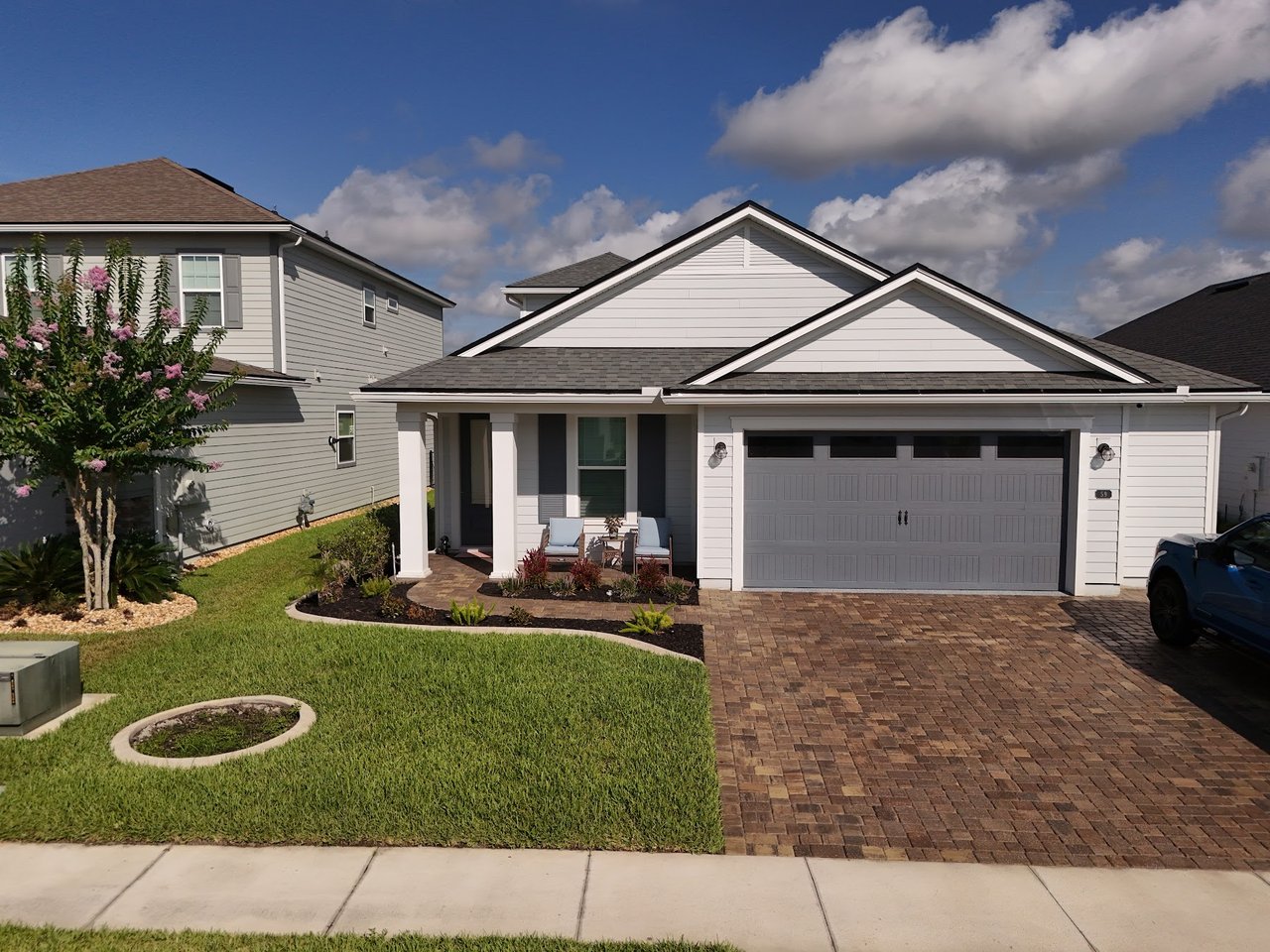 Single-story white home with a covered porch, double garage, and brick-paver driveway.