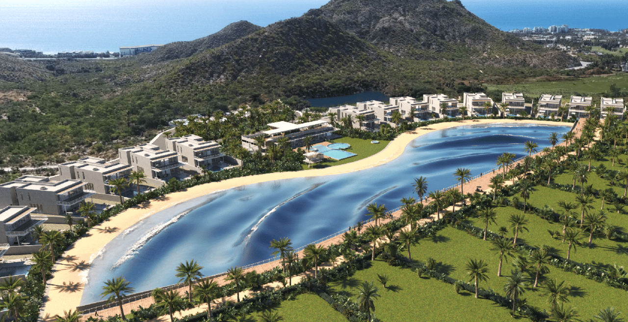 Coastal homes surround a blue lagoon and sandy beaches, with palm trees and rugged hills beyond.