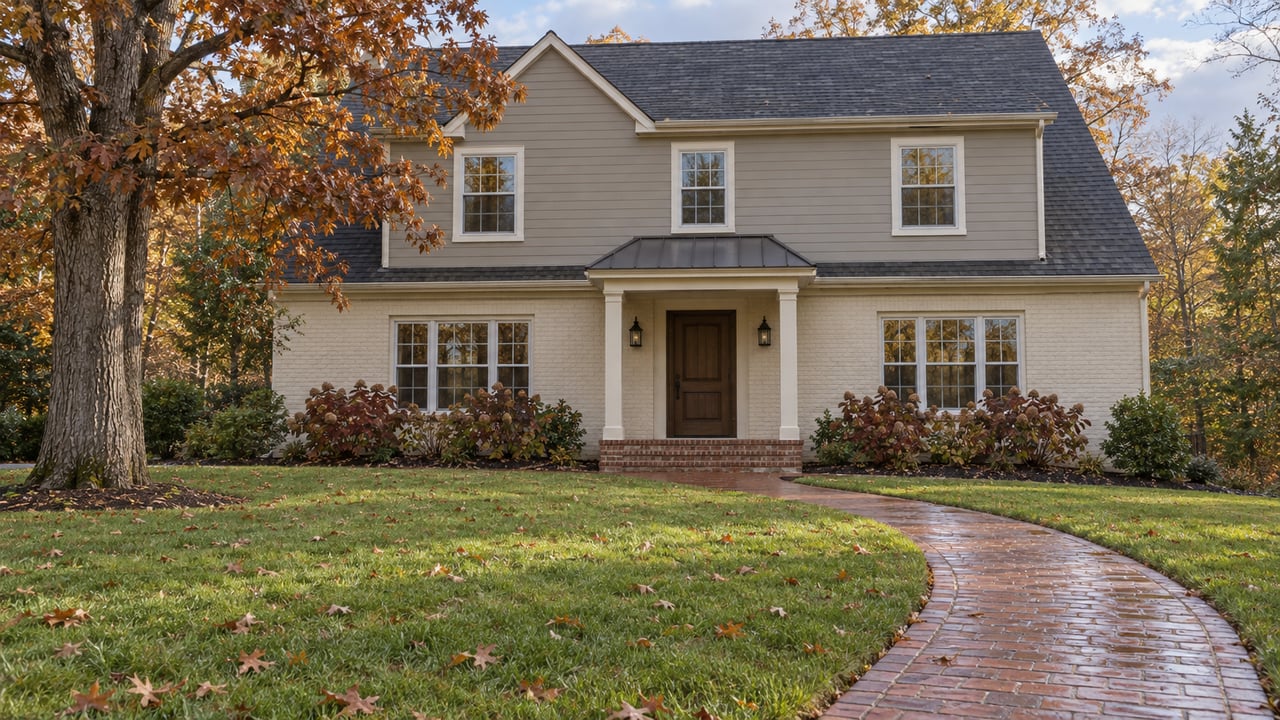 Two-story brick and siding home beyond a deep autumn lawn, with a curved brick walkway and a mature oak.