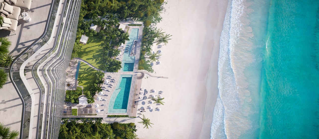 Aerial view of a beachfront residence with landscaped pool decks beside turquoise ocean.