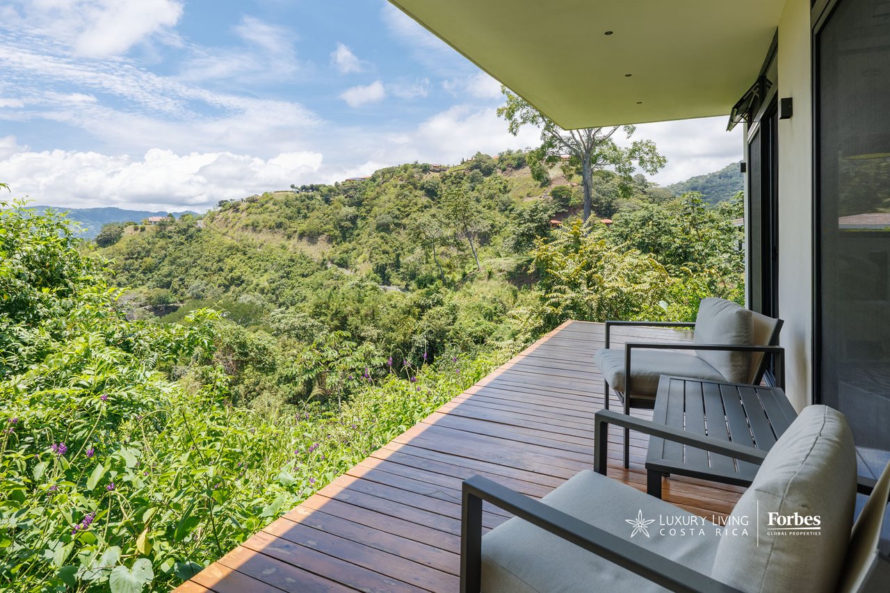 Modern home deck with lounge chairs overlooking a lush valley and rolling hills.