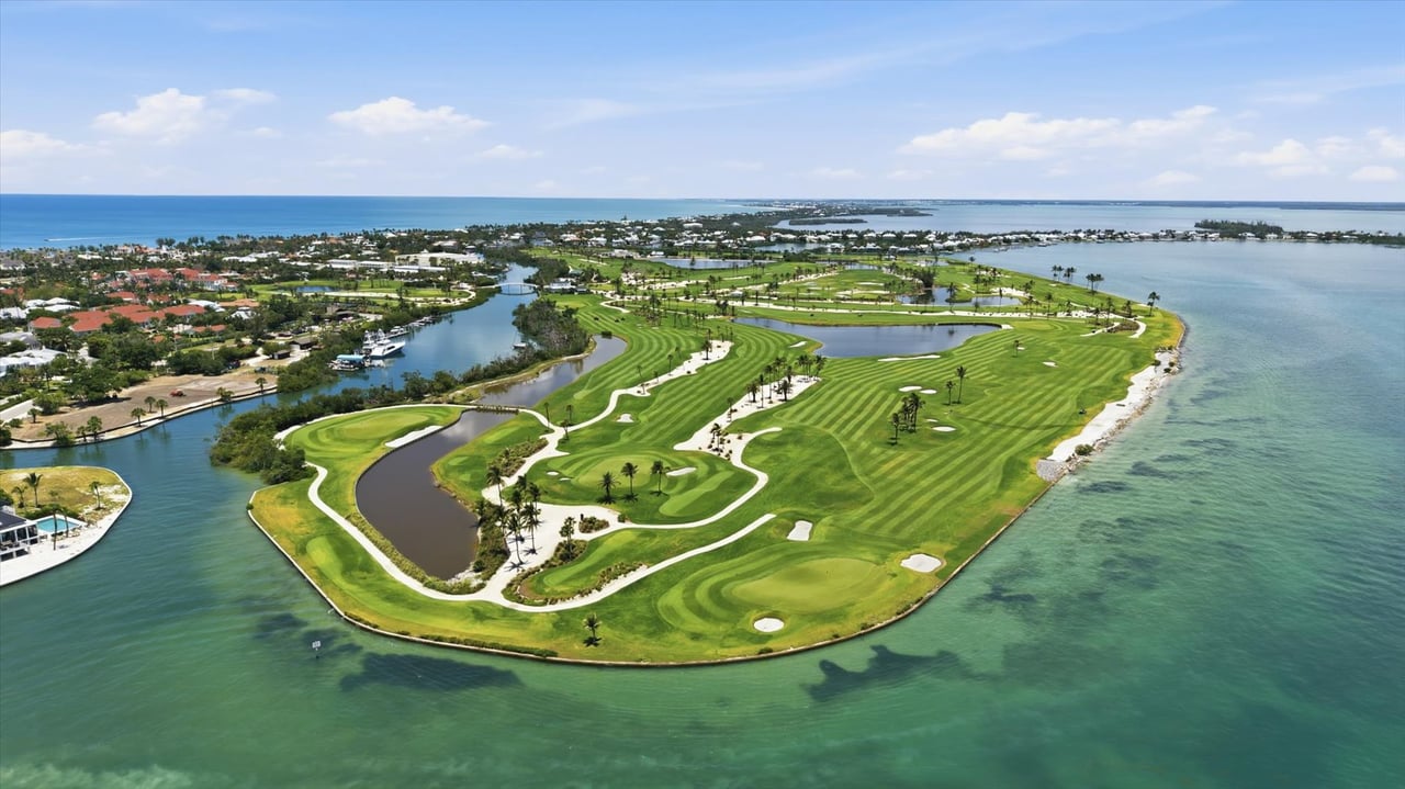 Coastal golf course peninsula surrounded by waterways, with striped fairways and nearby homes.
