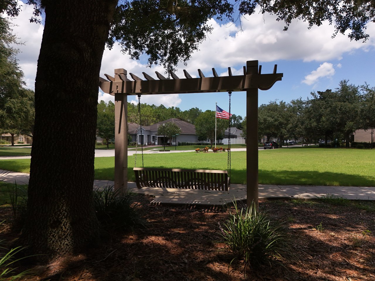 Neighborhood park with a pergola swing overlooking a green lawn and nearby homes.