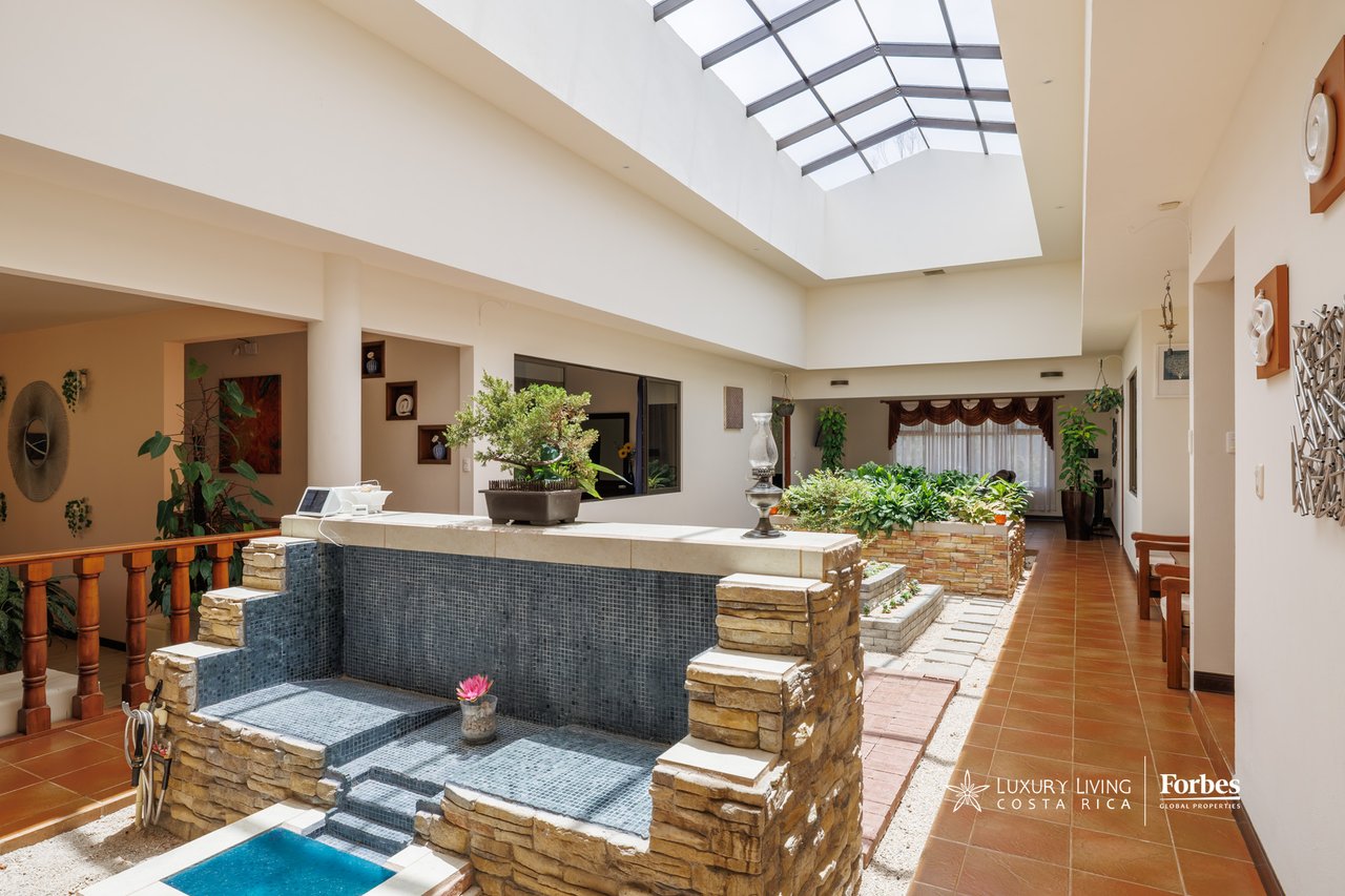 Indoor courtyard pool beneath a large skylight, with stone edging and lush plants.