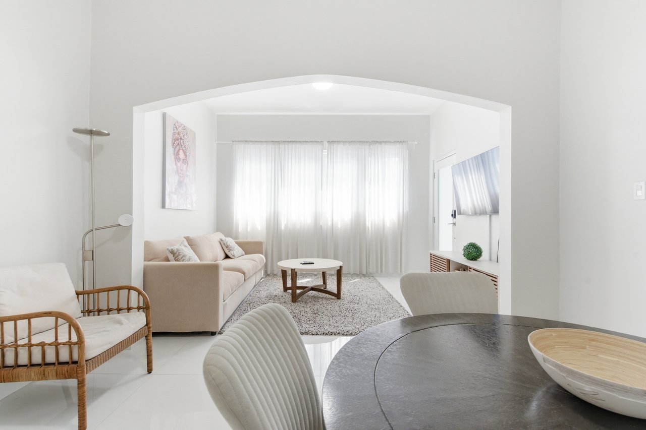 Furnished living and dining area with an arched opening, beige sofa, and sheer-curtained windows.