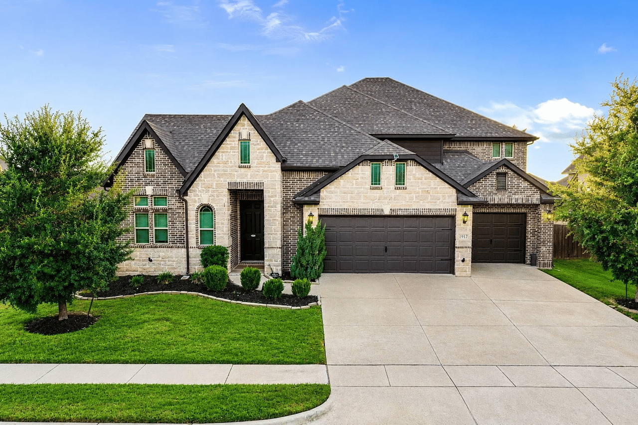 Two-story stone and brick home with multiple gables, a three-car garage, and landscaped lawn.