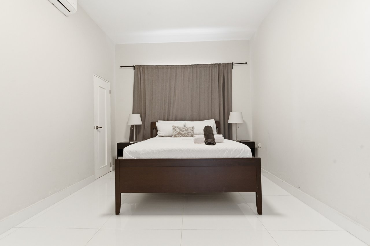 Furnished bedroom with a dark wood bed, white bedding, gray curtains, and matching bedside lamps.