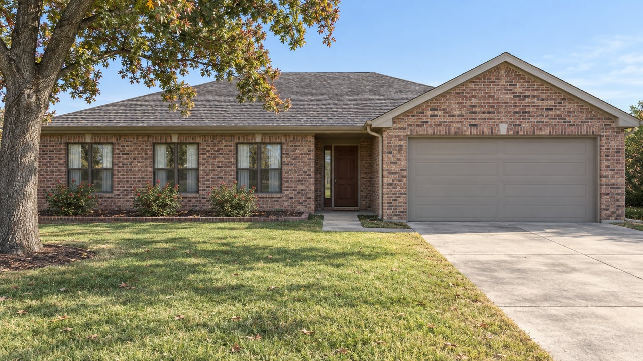 Red-brown brick single-story home with a charcoal gabled roof, attached garage, deep lawn and mature oak.