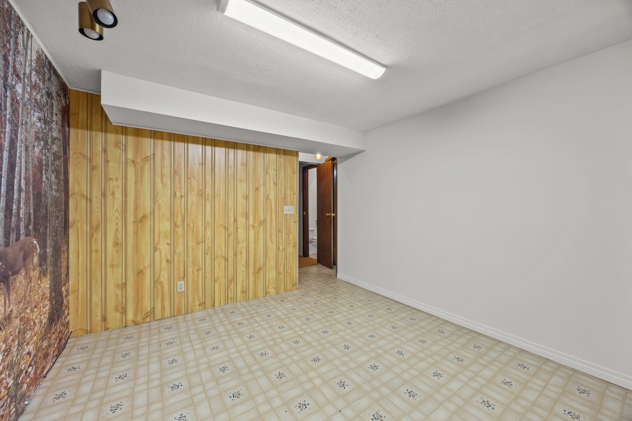 Empty room with wood-paneled walls, patterned tile flooring, and an open bathroom doorway.