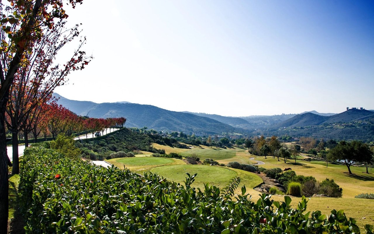 Golf course bordered by autumn trees, with rolling hills in the distance.