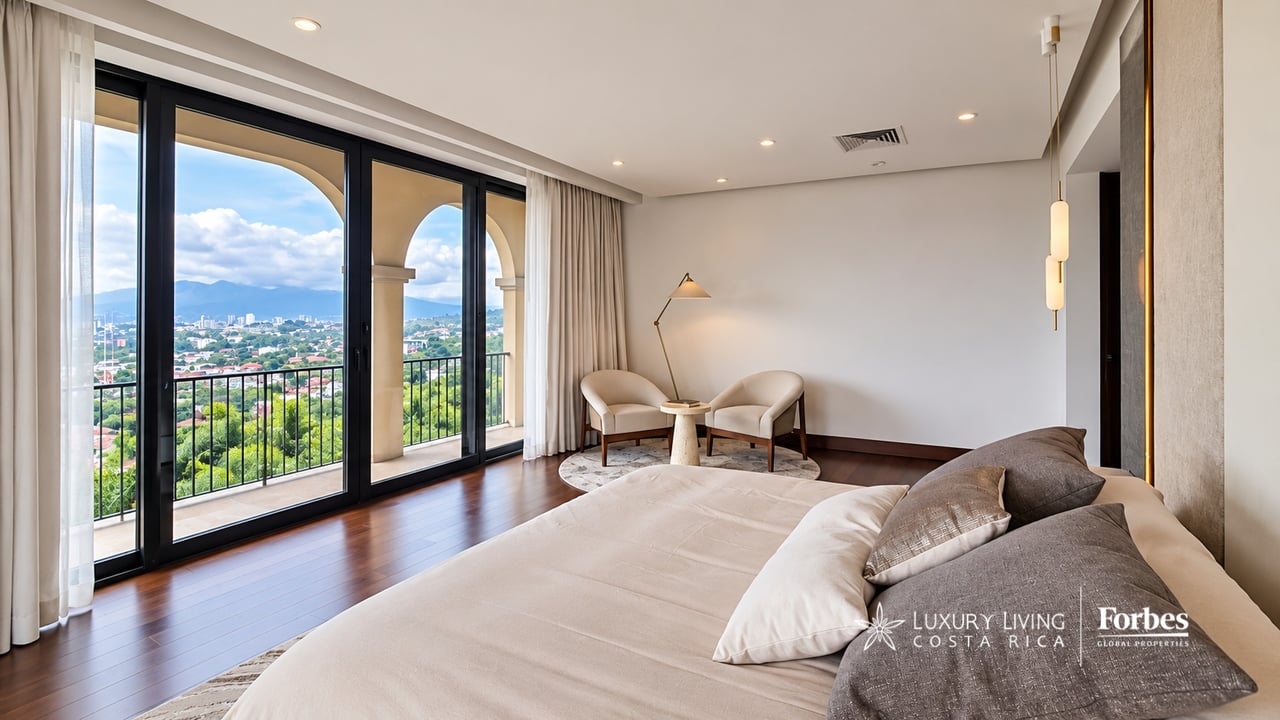 Penthouse bedroom with a large bed and armchairs, opening onto a balcony with city and mountain views.