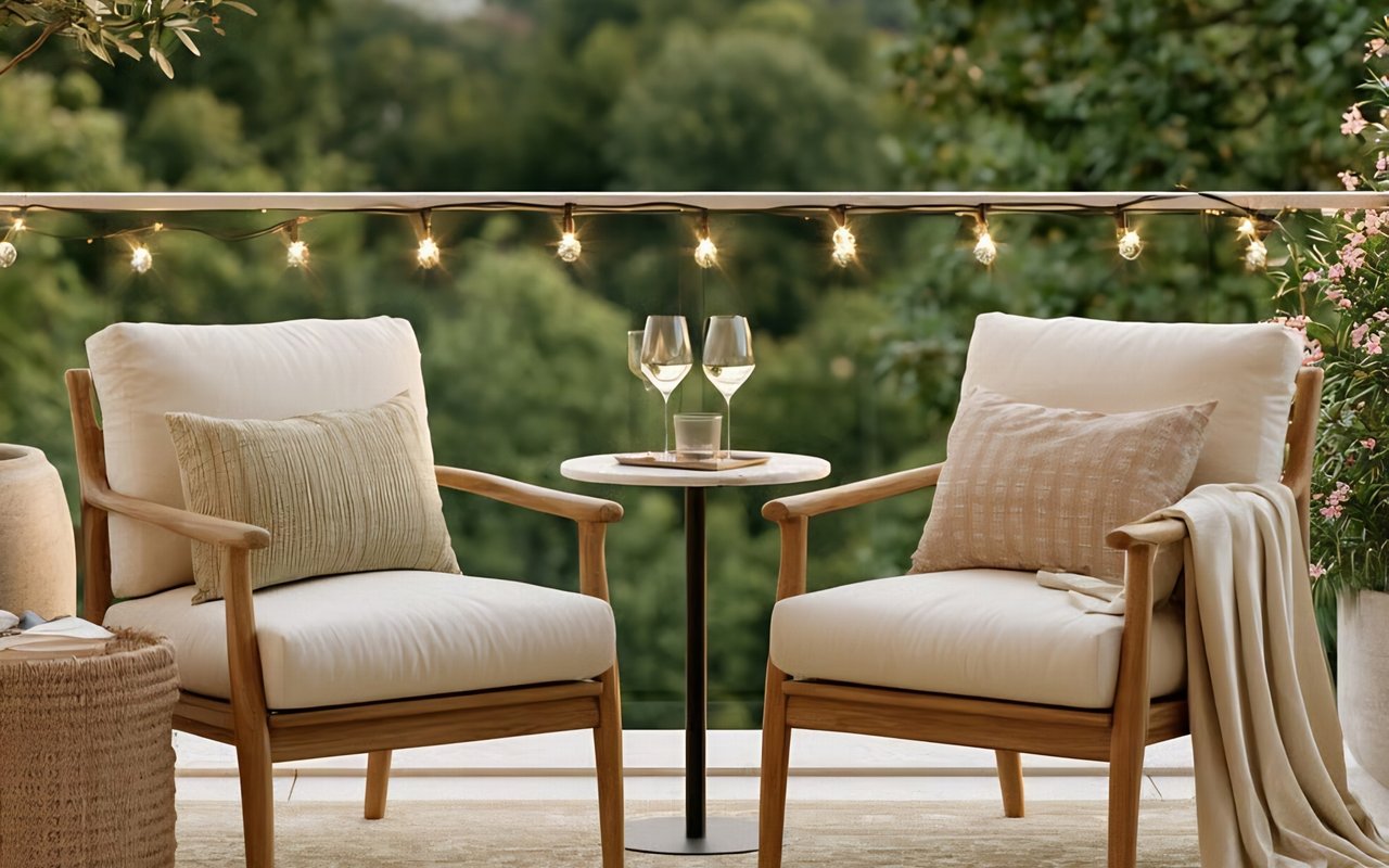 Outdoor patio with two cushioned wooden chairs, a small table, and string lights.