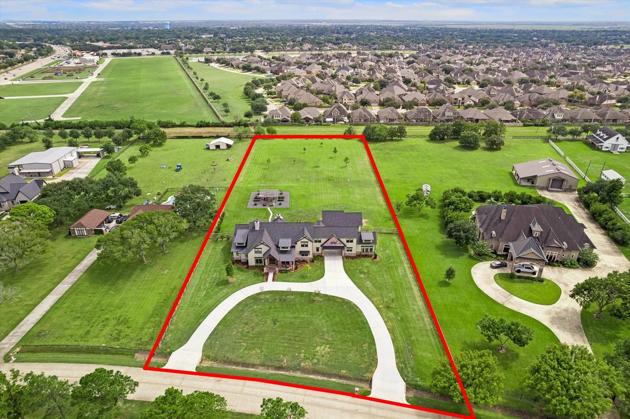Aerial view of a large green property with a house, curved driveway, and red boundary outline.