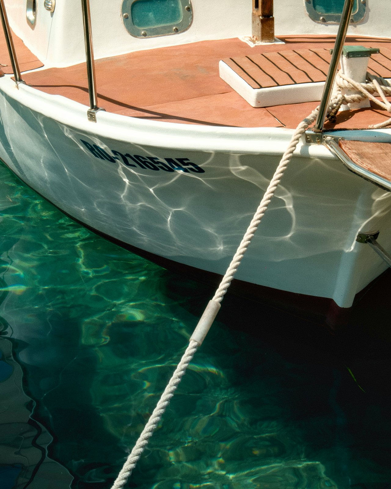 White MALIBU boat with a teak deck and mooring rope above clear turquoise water.