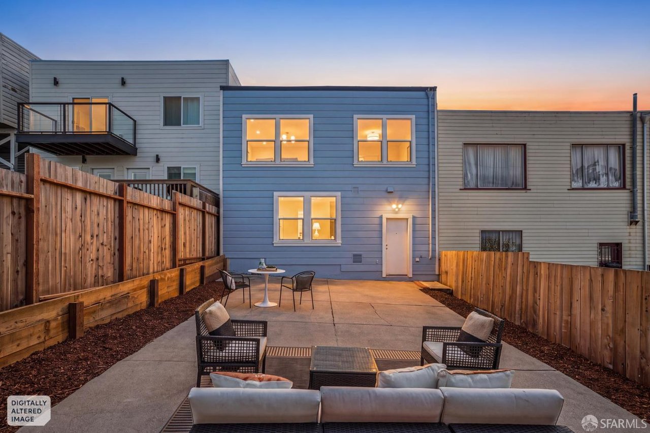 Modern home’s rear patio at dusk, with fenced concrete seating area and warmly lit windows.