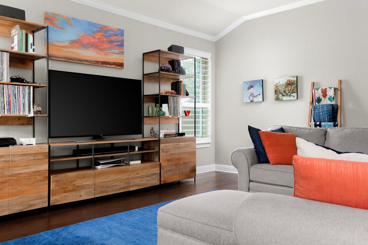 Living room with a large TV, wood shelving, gray sofa, and bright blue rug.