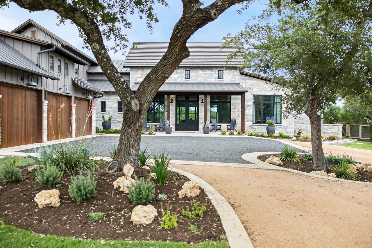Front elevation with stone and board and batten siding among mature oak trees at this Creek Road Ranch home in Dripping Springs, Texas, designed by architect Kai Geschke.