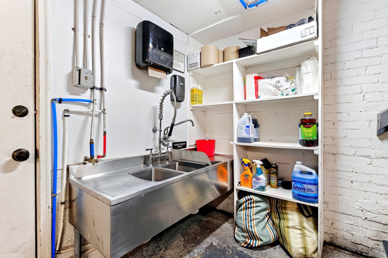 Restaurant utility area with a stainless-steel triple sink and shelves of cleaning supplies.