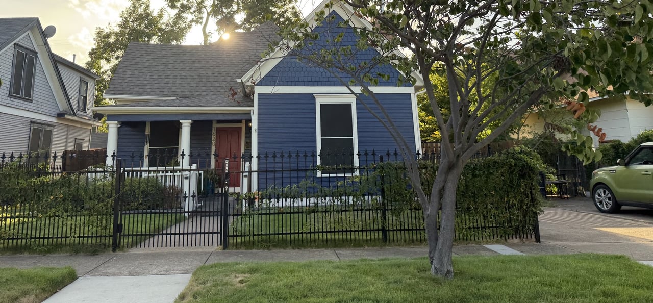 Blue house with a red front door, covered porch, and black iron fence.