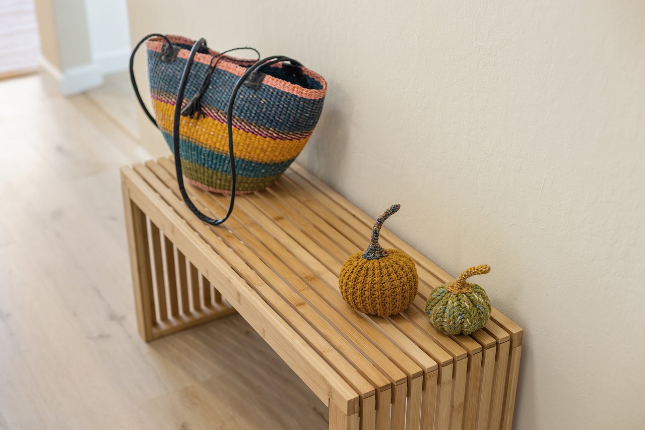 Colorful woven basket and knitted pumpkins sit on a slatted wooden bench.