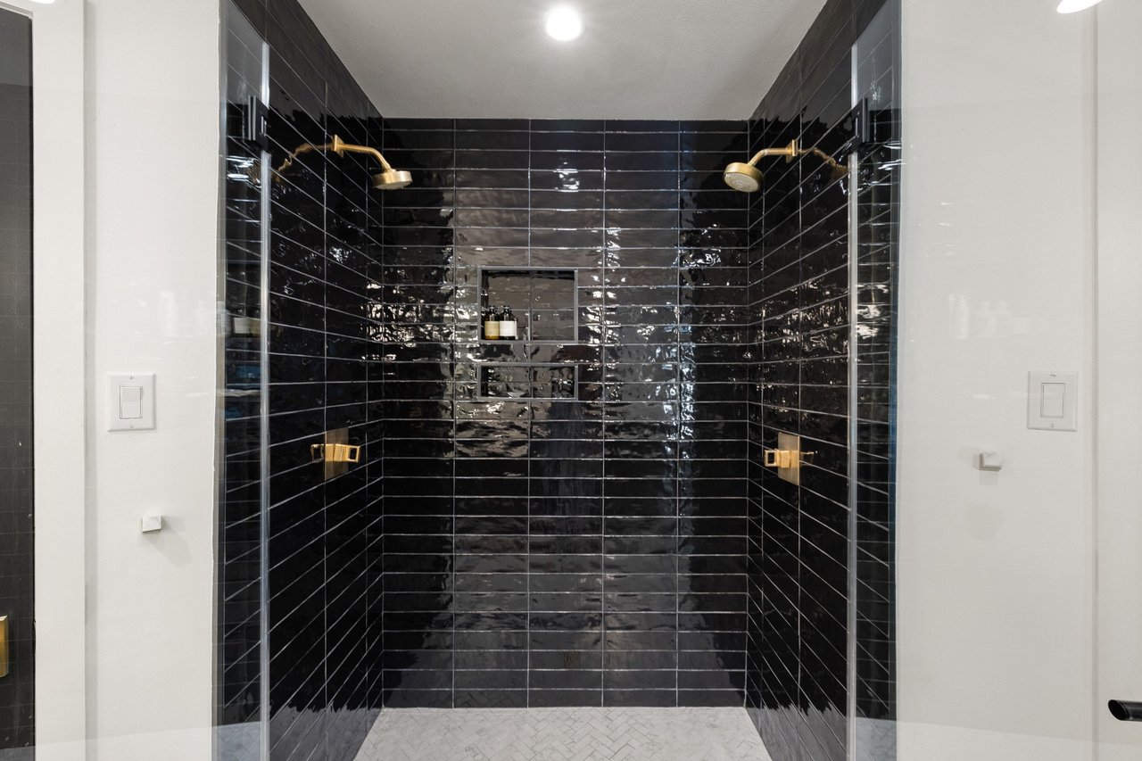 Walk-in shower with glossy black tile, brass fixtures, and a recessed shelf niche.