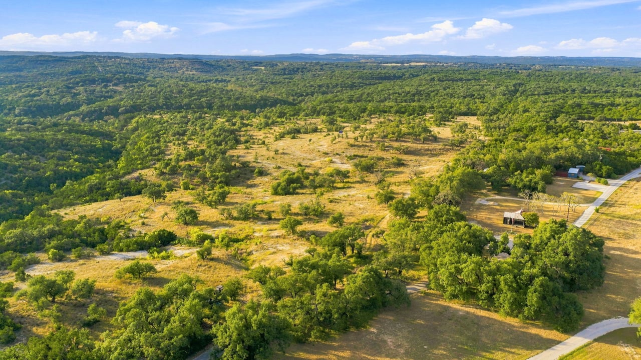 Aerial view of wooded ranchland with open clearings, a road, and scattered buildings.