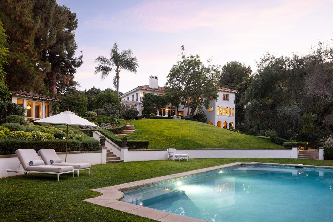 Mediterranean-style home overlooking a swimming pool and manicured lawn at dusk.